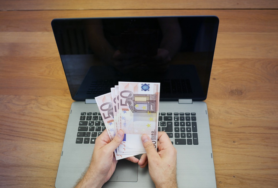 a person holding money and a laptop